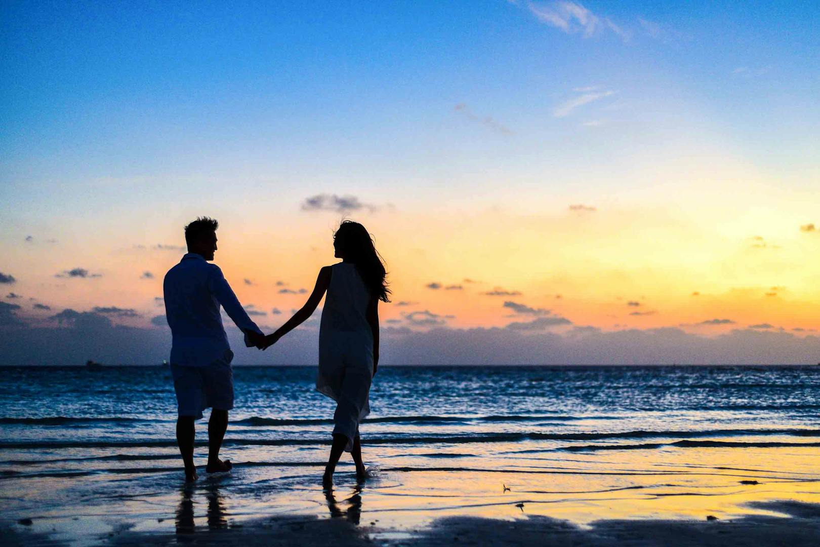 Couple holding hands at the shoreline during sunset